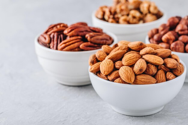 Almonds pecans walnuts and hazelnuts in white bowls on grey background Nuts mix Healthy food and snack Copy space