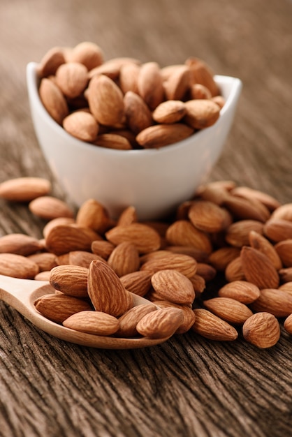 almonds in a white ceramic bowl with wood spoon on grained wood background