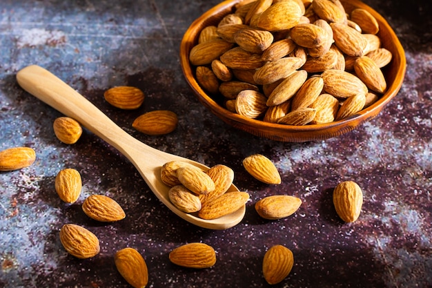 Almonds with wooden bowl and spoon on the dark table. 