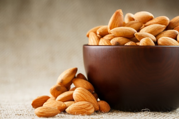 Almonds in a wooden cup on a burlap cloth background