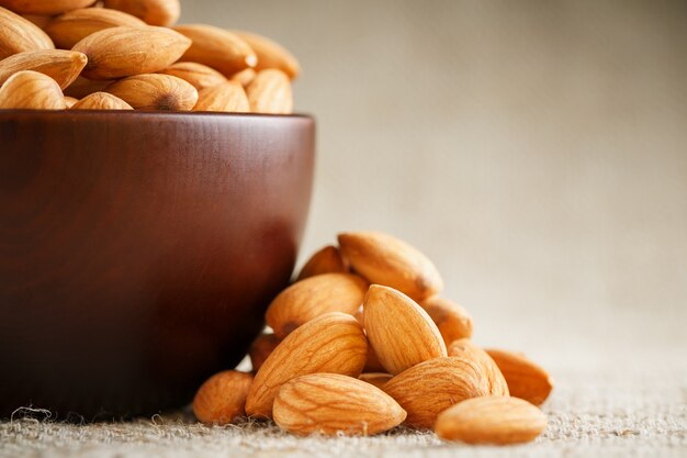 Almonds in a wooden cup on a burlap cloth background