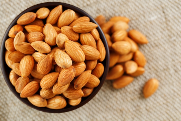 Almonds in a wooden cup on a burlap cloth background