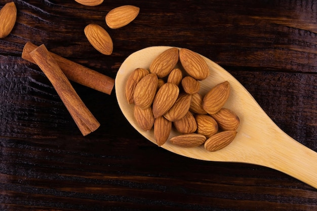 Almonds in a wooden spoon and cinnamon sticks, top view.