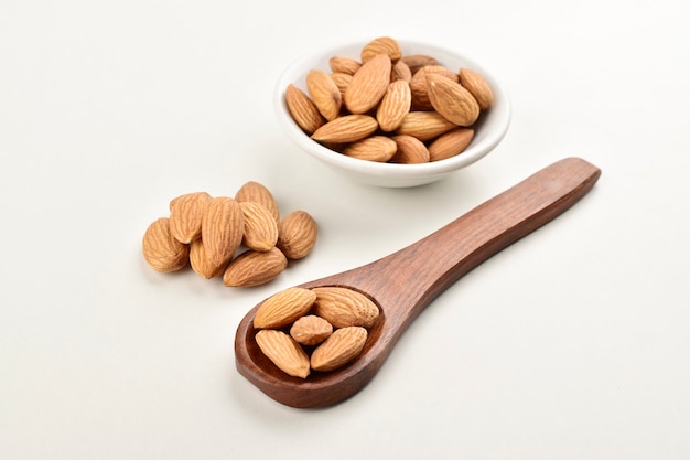 Almonds in wooden spoon and white bowl isolated on white background