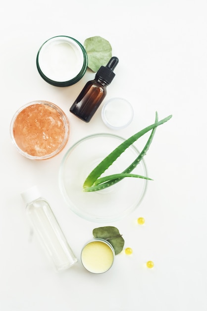 Foglie di aloe crema idratante, maschera e tonico su un tavolo bianco. creazione di prodotti di bellezza naturali a casa. miscelazione di estratti naturali per la produzione di siero antietà