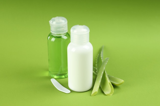 Aloe vera cosmetics and leaves on green background