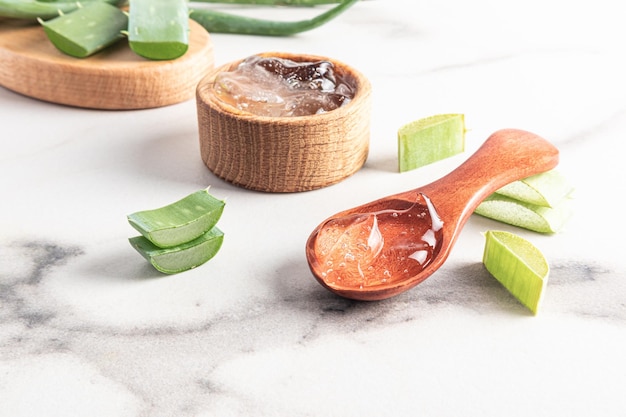 Aloe vera gel in a wooden spoon on a white marble table against a background of aloe leaves and a bowl of gel a natural cosmetic for selfcare