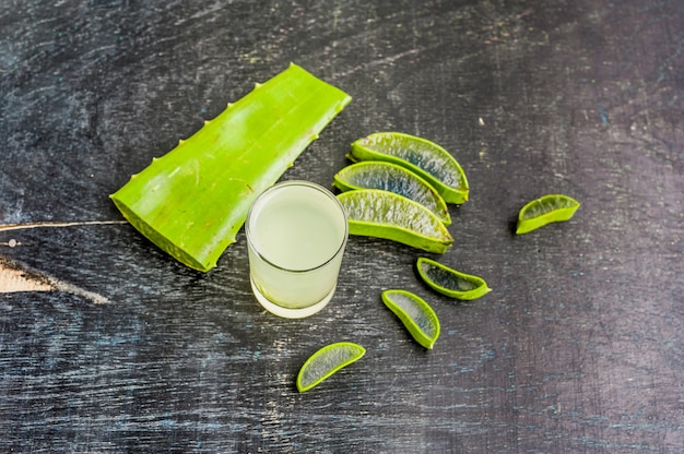 Aloe vera pieces and aloe gel in the glass on an old dark wood background