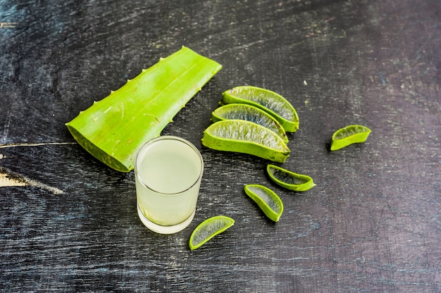 Aloe vera pieces and aloe gel in the glass on an old dark wood background