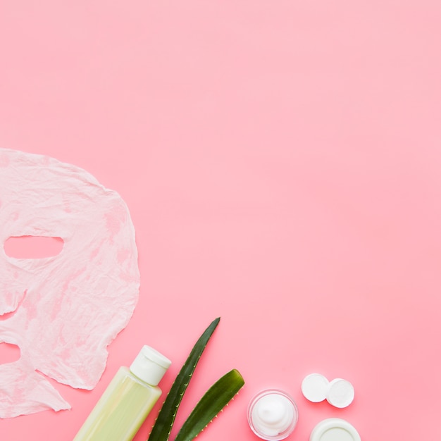 Foto crema per la pelle di aloe vera; lozione e maschera di foglio di carta sul fondale rosa