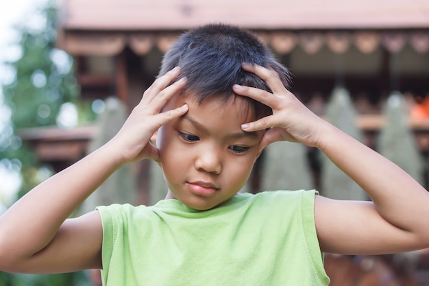 一人でアジアの小さな男の子は悲しみ、頭痛、ストレスを感じます。