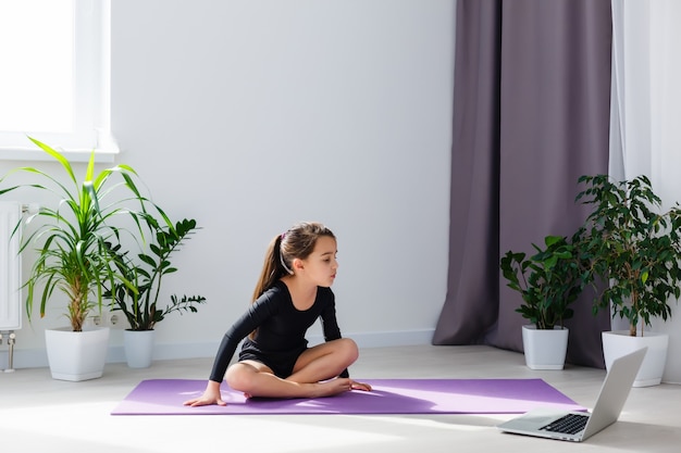 одна девушка делает упражнения йоги онлайн на ноутбуке на полу в светлой комнате, оставайтесь дома в безопасном мире.