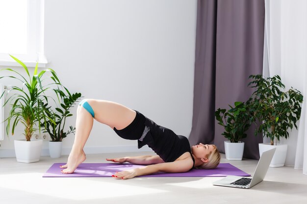 alone girl doing yoga exercises online on laptop on the floor in the light room, stay home safe world.