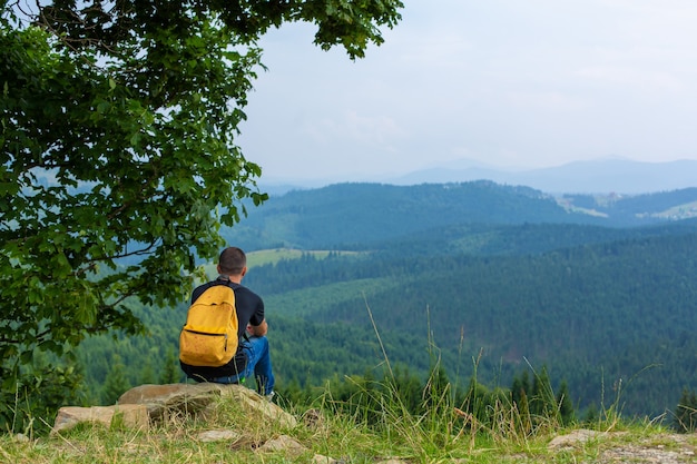 Alone guy sitting on cliff and enjoy peaceful green mountains landscape. Peace of mind and relax.