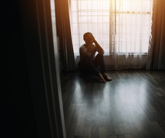 Одинокий мужской силуэт смотрит в окно, закрытое шторами в спальне