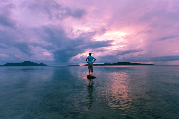 Alone man tourist standing on the stone in tropical sea and enjoying scenery during sunrise 