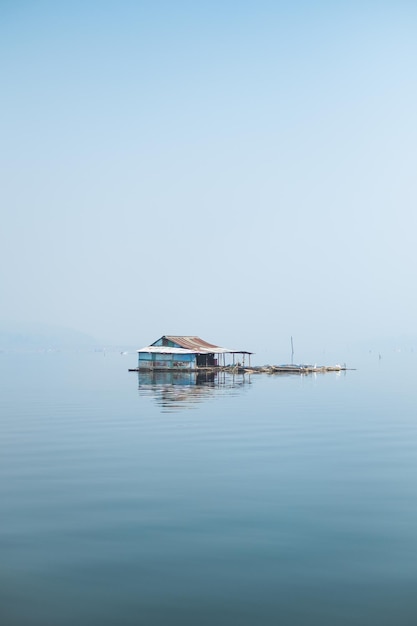 Foto vecchia casa di legno da sola che galleggia nel mezzo del lago blu e del cielo limpido