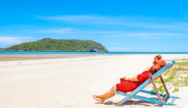 섬에서 바다와 하늘을 즐기는 열대 해변에서 나무 의자에 앉아 혼자 있는 여성