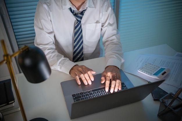 Alone Working Late at NightAsian business man at workplace in office holding his head on hands after late night work at a desk in a dark office working on a laptop late in the evening concept