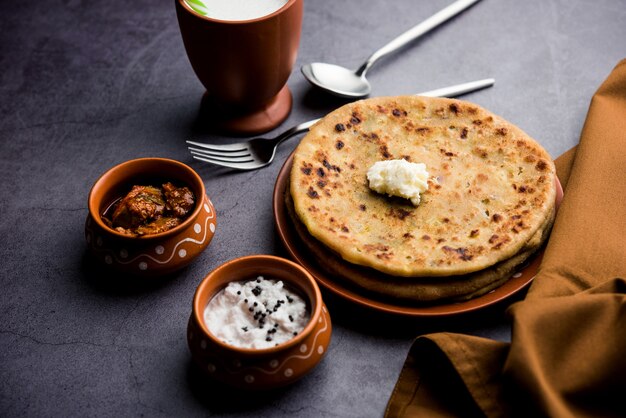 Aloo Paratha 또는 인도 감자 속을 채운 플랫브레드 위에 버터를 얹습니다. 신선하고 달콤한 라씨, 처트니, 피클과 함께 제공됩니다. 선택적 초점