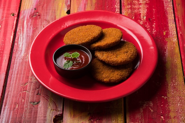 Aloo Tikki 또는 Patties 또는 Cutlet은 변덕스러운 배경 위에 토마토 케첩 또는 Imli 처트니와 함께 제공되는 인도의 인기 있는 스낵 또는 스낵입니다. 선택적 초점