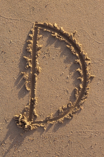 Foto lettere dell'alfabeto (d) scritte a mano nella sabbia sulla spiaggia