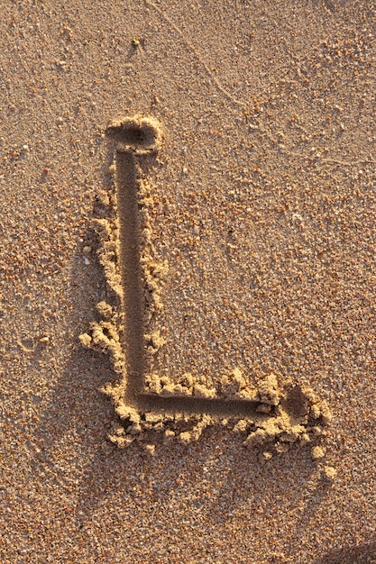 Lettere dell'alfabeto (l) scritte a mano nella sabbia sulla spiaggia