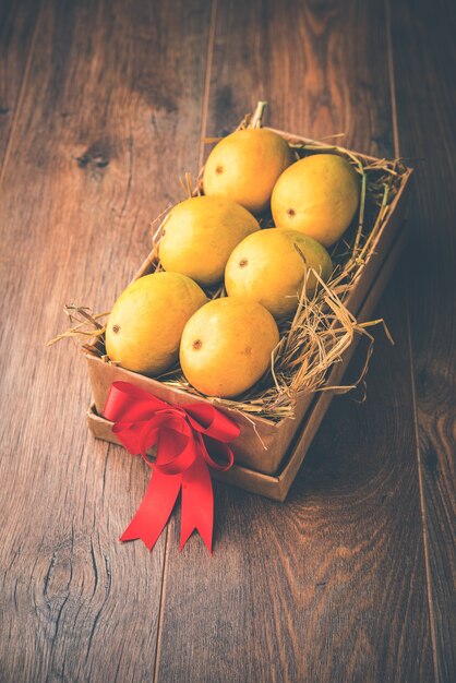 Alphonso mangoes in a gift box over grass and tied with red ribbon, selective focus