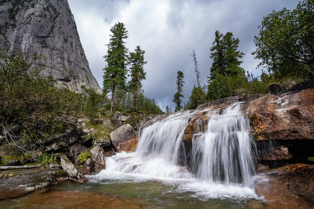 Alpine waterfall in mountain forest under blue sky.