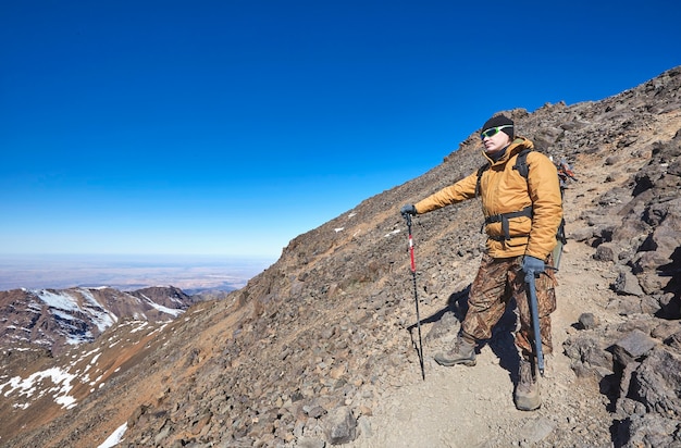 높은 아틀라스 산맥의 산악인. alpenstock, 얼음 도끼 및 관광 배낭과 함께 산에 선글라스에 백인 남자. 겨울 파노라마보기. 여행 사진.