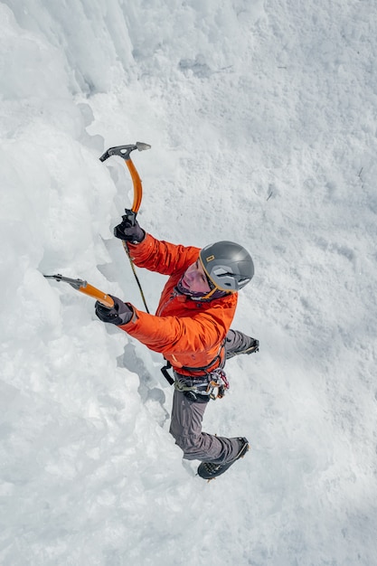 Alpinist man with ice tools axe climbing a large wall of ice. Outdoor Sports Portrait.