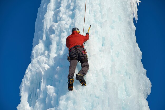 Alpinistische man met ijsgereedschap bijl beklimmen van een grote muur van ijs. Buitensport portret.