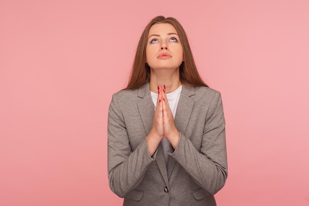 Alsjeblieft, god help. Portret van een smekende jonge vrouw in pak die opkijkt en bidt, smekend met gehoorzame smekende uitdrukking, gebaar van verontschuldigen. indoor studio-opname, geïsoleerd