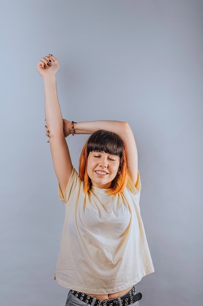 Alternatief Kaukasisch model met oranje haar dat een arm opheft en haar ogen in een positieve houding sluit.