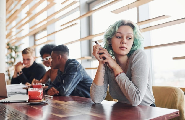 Foto alternatief meisje met groen haar zit tegen een groep multi-etnische mensen die binnenshuis aan tafel samenwerken.