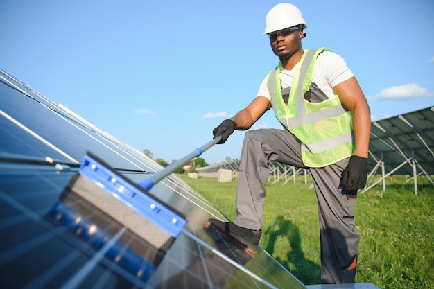 Alternatieve elektriciteitscentrale werknemer in uniform die zonnepanelen schoonmaakt met een mop Een knappe Afro-Amerikaan die voor de apparatuur zorgt