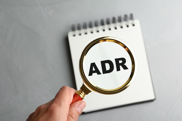 ライト グレーのテーブルでノートに略語 ADR の上に拡大鏡のガラスを保持している女性のクローズ アップ