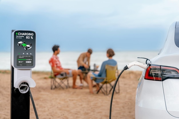 Alternative family vacation trip traveling by the beach with electric car recharging battery from EV charging station with blurred family enjoying the seascape background Perpetual