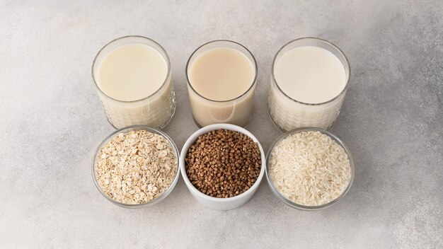 Alternative milk in glasses oatmeal buckwheat rice and bowls with an ingredient on a light background