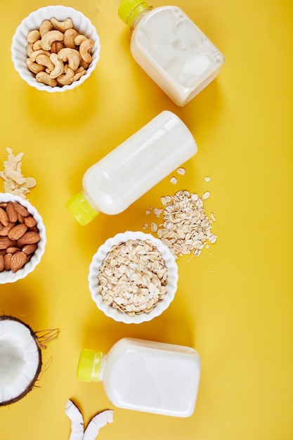 Alternative types of vegan milks in bottles on a yellow background, Various vegan plant based milk and ingredients, non-dairy milk