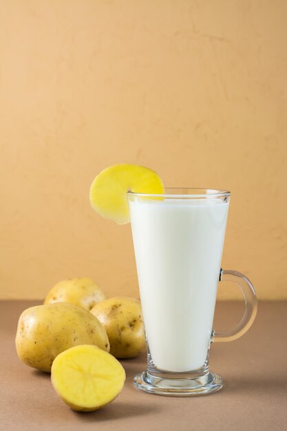 Alternative vegan vegetable potato milk in a glass and potato tubers next on a brown background. Vegetarian and flexitarian food. Vertical view. Copy space