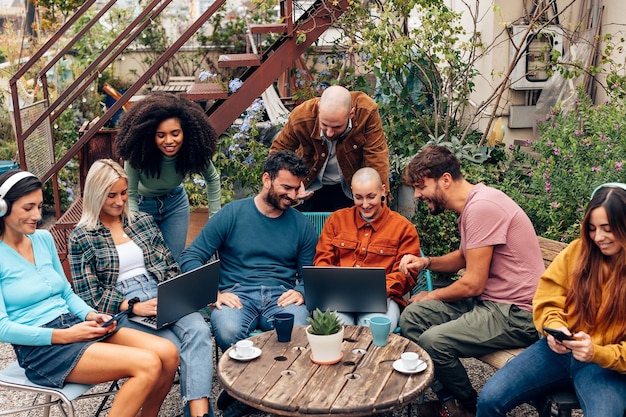 Ragazzi alternativi si siedono sulla terrazza dell'ostello della gioventù o del bar del dormitorio studentesco parlando e usando telefoni cellulari e laptop