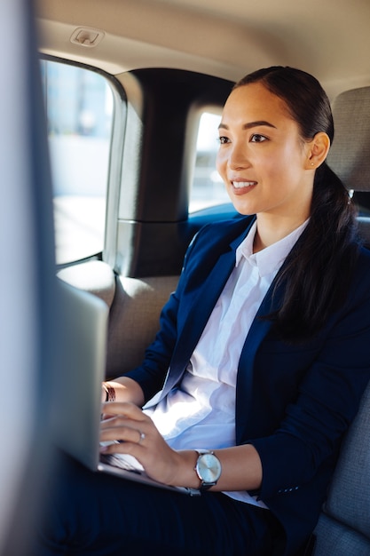 Altijd druk. Aangename zelfverzekerde zakenvrouw die op haar laptop werkt terwijl ze in de auto zit