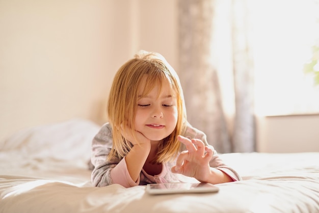 Altijd leuk online Shot van een klein meisje dat met haar tablet speelt terwijl ze thuis op haar bed ligt