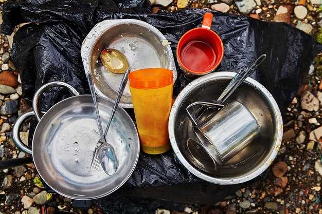 Aluminium kommen, borden, vork en lepel staan op de grond klaar voor het bereiden van voedsel in het bos.