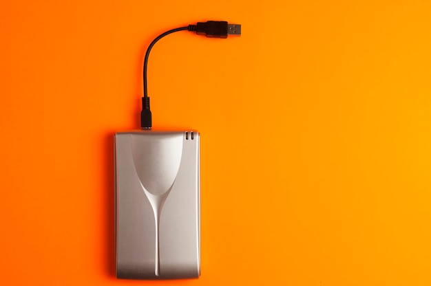 Photo aluminum external hard drive with connection cable usb orange background top view