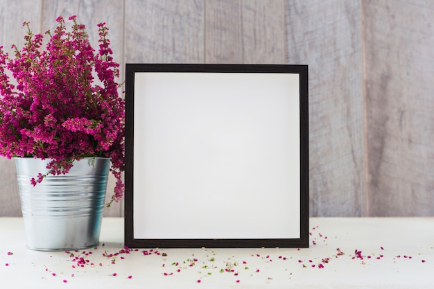 An aluminum pot with pink flowers and white square shape photo frame on table