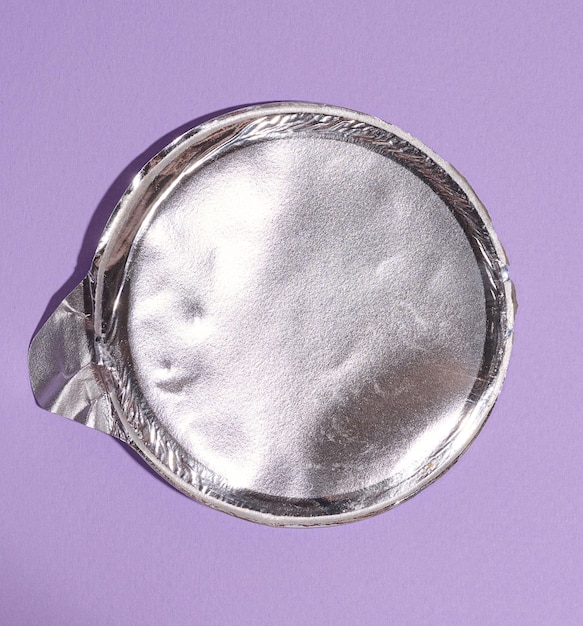 Aluminum round lid from under the package with chips on a purple background flat lay