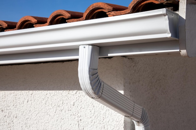 Photo aluminum white gutter on the roof of the building and downpipe on the wall