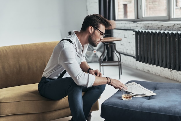 Always aware of latest news. stylishly dressed young man reading a newspaper while sitting on sofa